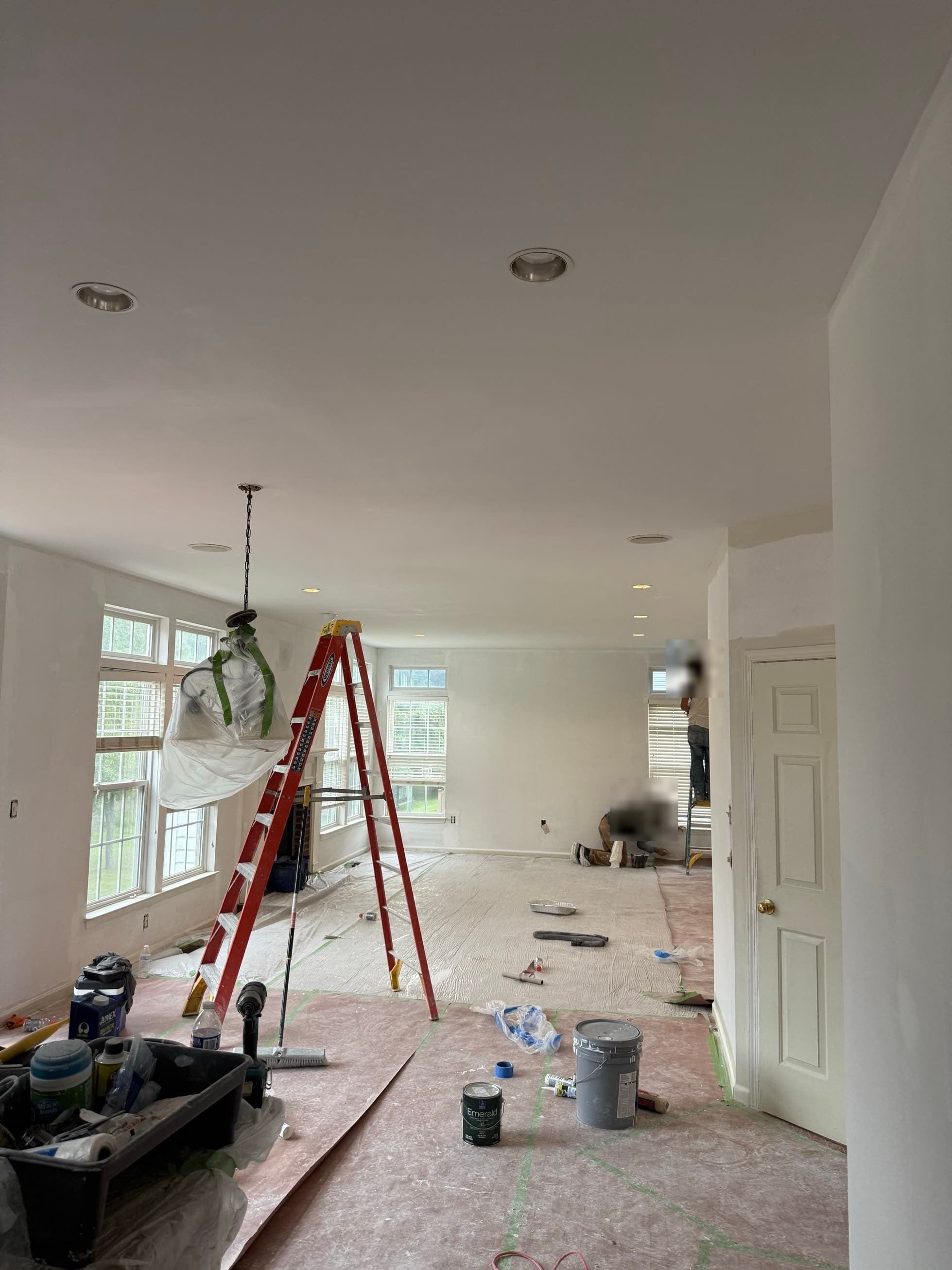 A crew painting and smoothing ceilings in a fully masked great room